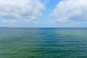 Fototapeta premium Calm Teal Ocean Waters Extend to the Horizon Beneath a Bright Blue Sky with Fluffy Clouds Serene seascape scenery depicts tranquil ocean views for background stock
