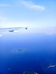 Fototapeta premium Serene aerial view from an airplane, with a portion of the white aircraft wing visible. Below, the vast expanse of deep blue ocean stretches out, dotted with several lush green tropical islands