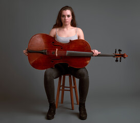 Young female musician holding a cello while sitting on a stool
