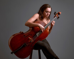 Young woman musician playing cello in studio with gray background