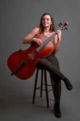 Young female musician playing cello sitting on stool in studio