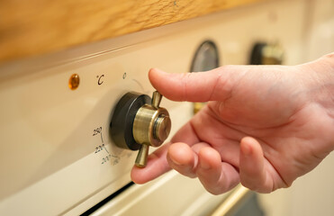 Hand adjusts temperature dial on an oven at home kitchen while preparing a meal or baking
