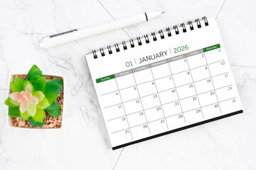 Desk calendar on month of January 2026 with pen on white marble background.
