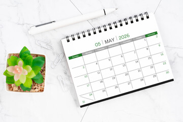 Desk calendar on month of May 2026 with pen on white marble background.