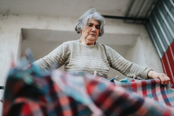 A senior woman holding and arranging a bright plaid textile while being outside, showcasing...