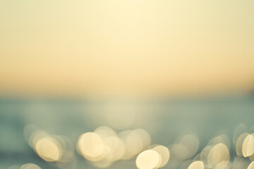 softly blurred seascape at sunset, featuring golden light reflections dancing across the water in a warm, serene atmosphere.