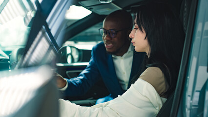 A car dealer in a modern car dealership advises a customer on buying or leasing a new car. The...