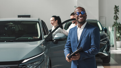 A couple during the purchase of a modern new car accompanied by a black salesman in a car dealership. Concept of a long-awaited purchase, sale and test drive of a new car.