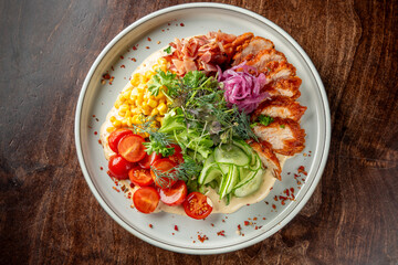 A plate of assorted food featuring sliced grilled chicken, diced ham, corn kernels, cherry tomatoes, pickled onions, cucumber slices, and fresh herbs on a creamy sauce, presented in an appetizing and 