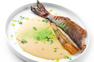 Grilled fillet dorado fish with sauce and greens on the plate isolated on white background. Healthy seafood, top view, close up