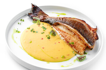 Grilled fillet dorado fish with sauce and greens on the plate isolated on white background. Healthy seafood, top view, close up