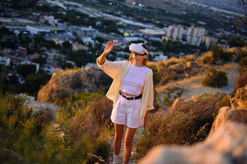 Woman exploring nature with virtual reality headset on hilltop at sunset