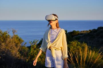 Woman exploring nature with virtual reality headset at sunset by the ocean