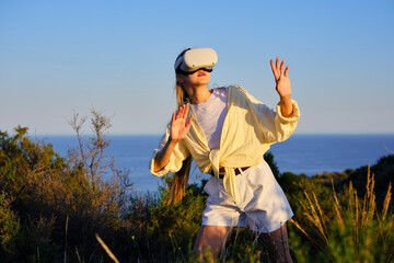 Woman in virtual reality headset exploring nature at sunset by the sea