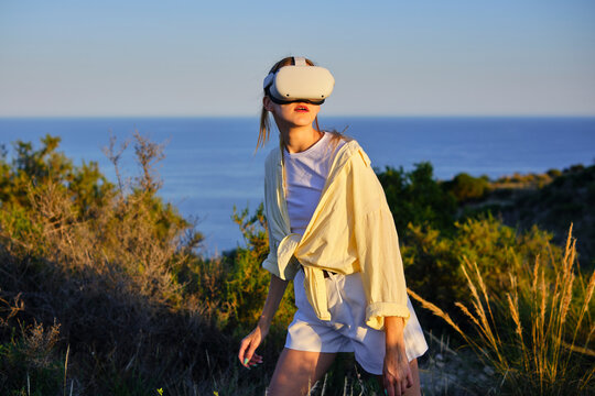 Woman exploring nature with virtual reality headset near the ocean at sunset - Powered by Adobe