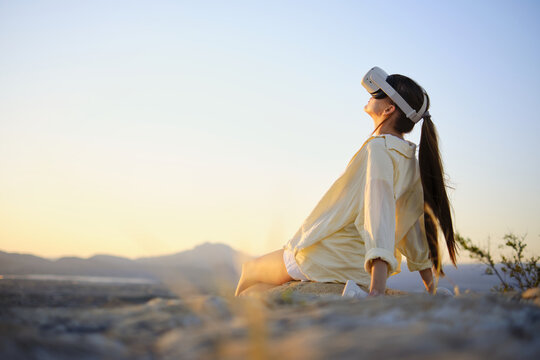 Woman relaxing outdoors wearing virtual reality headset at sunset