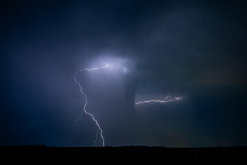 A strong storm is approaching with fierce bolts of lightning illuminate ominous clouds.