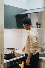 A person prepares a meal on the stove top inside a modern, well-lit home kitchen setting. The scene highlights cooking, food preparation, and domestic activity.