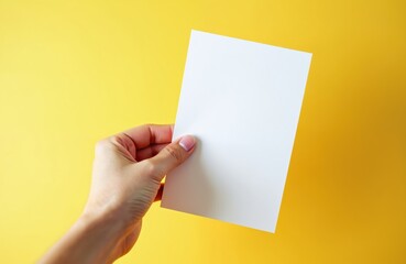 Hand holding blank white greeting card mockup against yellow background. Invitation letter poster flyer template for design, presentation. Ideal for business message, information, promotion.