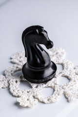 Black chess knight on a white crochet doily © Mariia