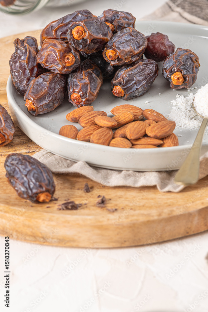 Aufkleber medjool dates and almonds on a plate with a spoonful of shredded coconut, set on a wooden board with