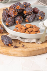 Medjool dates and almonds on a plate with a spoonful of shredded coconut, set on a wooden board with a jar of dates in the background