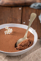 Silky chocolate mousse in a white bowl, a spoonful being lifted, decorated with tiny white flowers,...