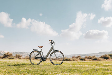 Fototapeta premium sleek electric bicycle parked on lush green meadow surrounded by gentle hills and occasional fluffy clouds in sky