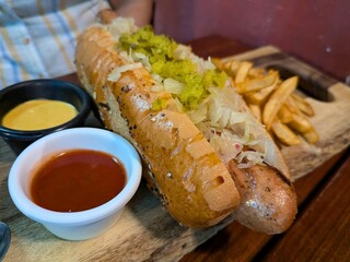 Gourmet hot dog with sauerkraut, diced pickles, and artisan bun, served with fries, mustard, and ketchup. A bold and hearty American-style meal.