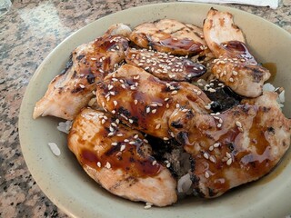 Close-up of grilled chicken teriyaki bowl with sesame seeds and seaweed on steamed rice. Perfectly glazed chicken pieces for a rich, flavorful experience.