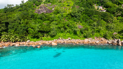 The vibrant meeting of turquoise waters and rugged rocky shores flanked by dense greenery. Praslin, Seychelles.