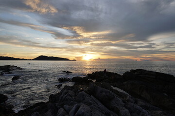 Obraz premium Serene Sunset Over Rocky Shoreline with Calm Ocean and Dramatic Sky Colors at Dusk