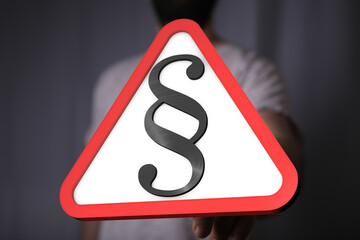 Stock photo of a hand holding a red triangle warning sign with a paragraph symbol.  Perfect for...