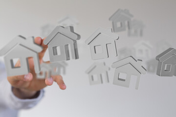 A hand interacts with floating 3D house models, symbolizing real estate, property, or home...