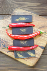Bar of extra dark chocolate with three red chili peppers on a wooden cutting board on the table. Trend food concept. Selective focus. Vertical orientation