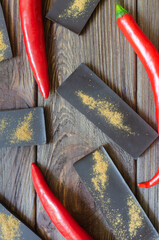 Bar of extra dark chocolate with three red chili peppers on a wooden table. Trend food concept. Selective focus. Vertical orientation. Top view