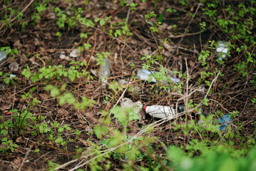 Plastic bottles and garbage scattered among dry branches and spring plants in the forest. Symbol of environmental pollution, ecological problems and human impact on nature.
