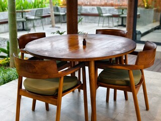 A round wooden dining table set with four matching wooden chairs in an outdoor cafe