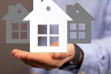 Image of a real estate agent's hand holding house models, symbolizing home buying, selling, or investment.