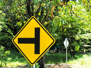 A warning traffic "Intersection sign" (Warning sign for a secondary road intersection to the left). Control traffic to be orderly. Yellow Steel sign with black border and letters. Traffic Signs Vocab
