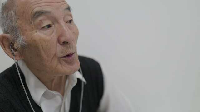 Elderly man wearing earphones talking on white background