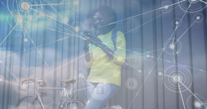 Image of network of connections over clouds and african american woman with smartphone and bike