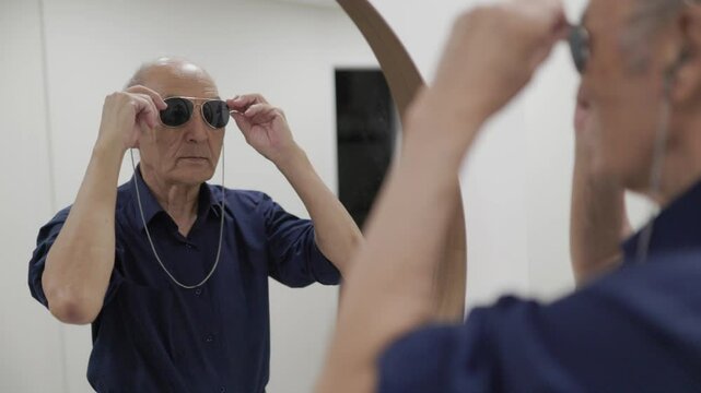Senior man trying sunglasses in front of mirror