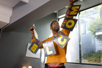 African American man moving WELCOME banner under slanted beam in living room with canvas and lamp