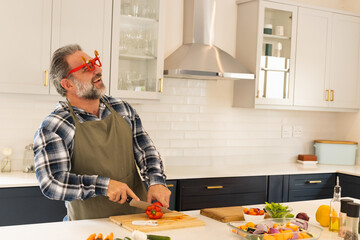 Middle-aged man holding chef's knife slicing red bell pepper on cutting board at kitchen island