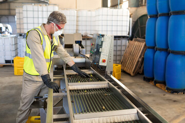 Conveyor belt transporting small green produce through warehouse facility with barrels and crates
