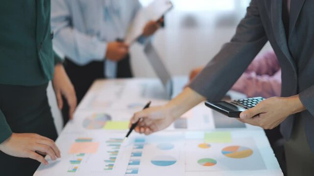 A group of young asian business people working together and double checking the company's profits shown in graphs and charts to prepare for the meeting soon