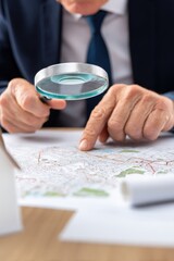 Person examining a map with a magnifying glass in a professional setting