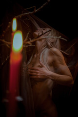 Obraz premium Beautiful blonde woman posing in brown veil by candlelight on dark background, gothic queen, art style..