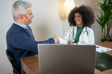 Woman doctor shaking hand with male patient in the office. Doctors are encouraging patients. Doctor and patient shaking hands. Diverse healthcare